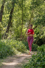 Evy Gruyaert from Start to Run in a sustainable pure by luce activewear outfit running in a forest: red printed Naomi Cape Town leggings and Gugu Red sports crop top