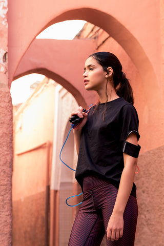 pure by luce sustainable Yattou Black sports T-shirt with cut-out sleeves and dark red all-over printed Alou Marrakech leggings worn by a ropeskipping girl in Morocco