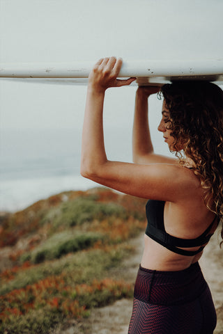 pure by luce sustainable Charo Black bra top: black low-support sports bra with cross back and dark red all-over printed Alou Marrakech leggings feauturing a surfboard at the beach
