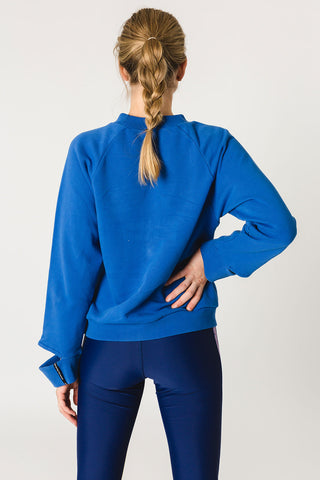 pure by luce sustainable athleisure Nina Blue sweater with cut-out sleeve cuffs and logo detail with dark blue shiny Rene Paarl leggings