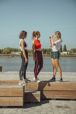 three girls in sustainable pure by luce outfits: dark red Rene Cape Town leggings with printed side stripes with the Gugu Red sports crop top and blue all-over printed Shourouk Akchour loose running shirts with the Yattou White sports T-shirt with cut-out sleeves and black Rene Joburg leggings with printed side stripes with the Rehanna White cutout sports top
